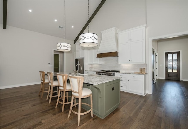 kitchen featuring high vaulted ceiling, custom exhaust hood, a kitchen island with sink, decorative backsplash, and stove