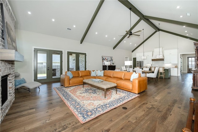 living area featuring visible vents, high vaulted ceiling, ceiling fan, dark wood-type flooring, and a large fireplace