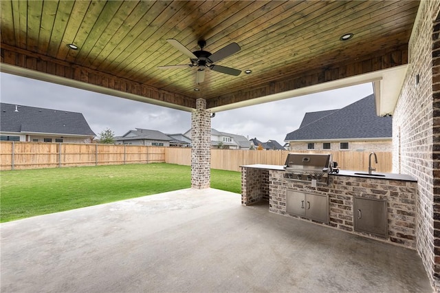 view of patio / terrace featuring a fenced backyard, an outdoor kitchen, a grill, a ceiling fan, and a sink