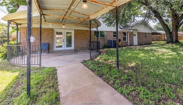 entrance to property featuring a lawn, a patio area, french doors, and central air condition unit