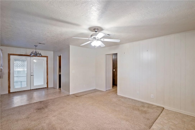 unfurnished room with french doors, a textured ceiling, light colored carpet, ceiling fan, and wood walls