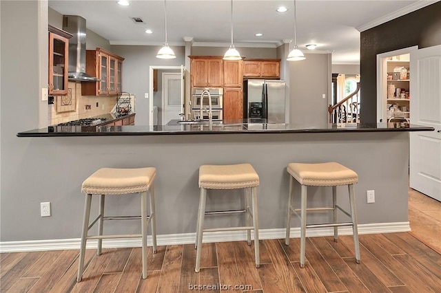 kitchen with hanging light fixtures, light hardwood / wood-style flooring, wall chimney exhaust hood, kitchen peninsula, and stainless steel appliances