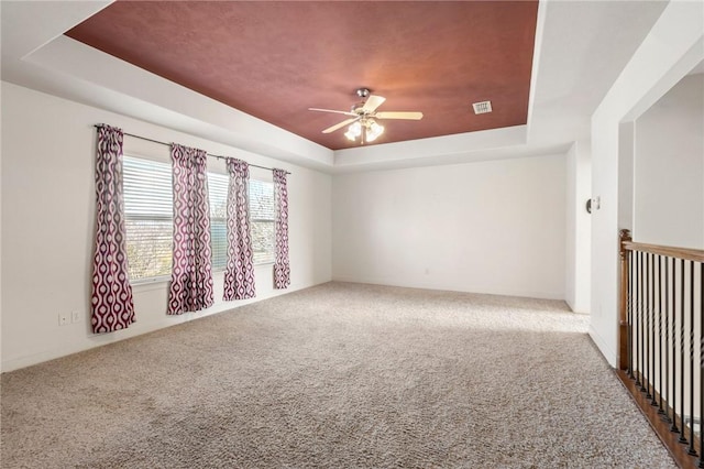 spare room with ceiling fan, a tray ceiling, and carpet floors