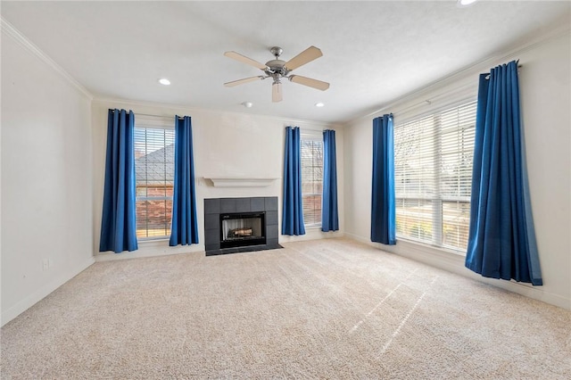 unfurnished living room with ceiling fan, light colored carpet, ornamental molding, and a tiled fireplace