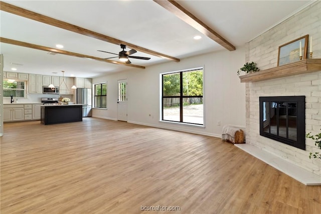 unfurnished living room featuring ceiling fan, beam ceiling, light wood-type flooring, and a fireplace