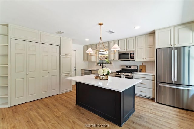 kitchen with pendant lighting, a kitchen island, stainless steel appliances, and light hardwood / wood-style floors