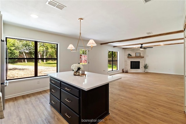 kitchen featuring a brick fireplace, a kitchen island, beam ceiling, decorative light fixtures, and light hardwood / wood-style floors