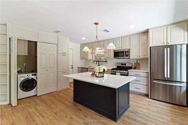 kitchen with stainless steel appliances, decorative light fixtures, washer / dryer, a kitchen island, and light wood-type flooring