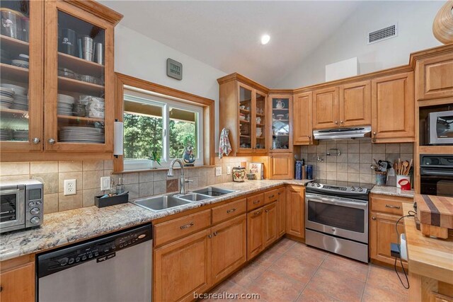 kitchen featuring light tile patterned flooring, appliances with stainless steel finishes, lofted ceiling, sink, and light stone countertops