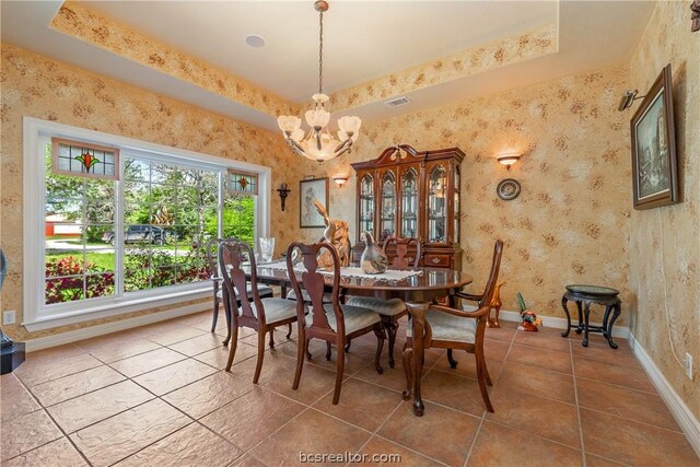 dining space featuring an inviting chandelier, a raised ceiling, and tile patterned flooring