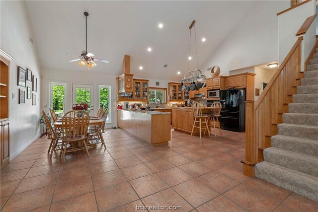 kitchen featuring a kitchen island, stainless steel microwave, high vaulted ceiling, a kitchen breakfast bar, and black fridge with ice dispenser