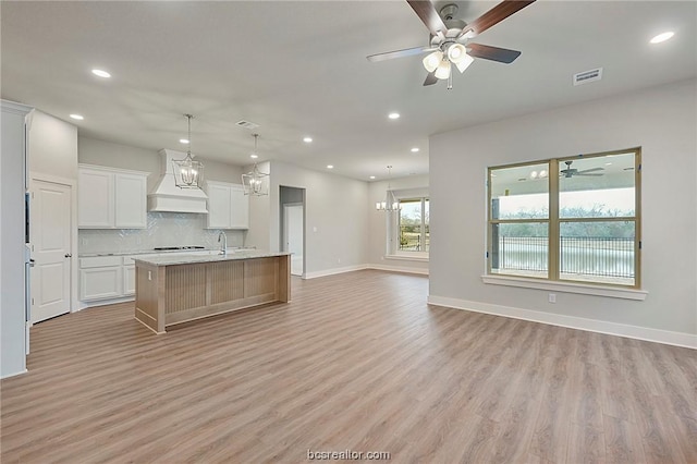 kitchen with a kitchen island with sink, premium range hood, light hardwood / wood-style flooring, decorative light fixtures, and white cabinetry