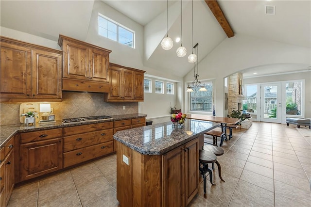 kitchen featuring pendant lighting, dark stone countertops, backsplash, a center island, and stainless steel gas stovetop