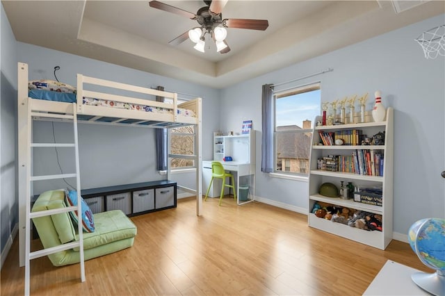 bedroom with hardwood / wood-style floors, ceiling fan, and a tray ceiling