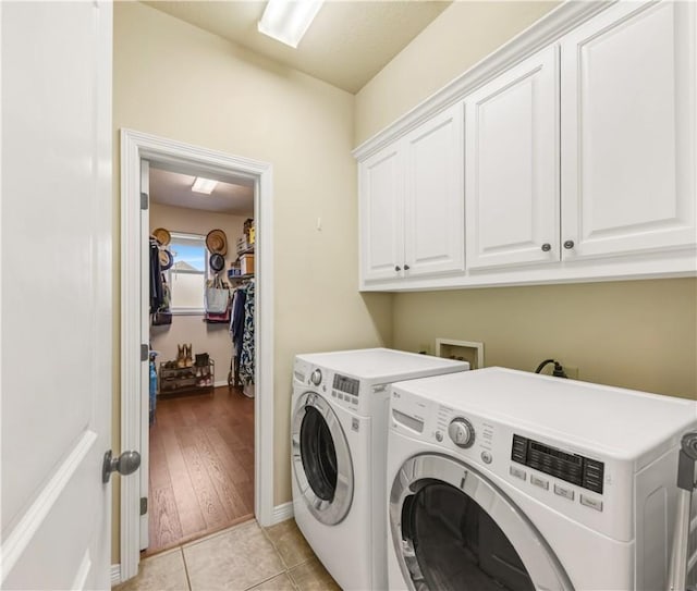 clothes washing area with cabinets, light tile patterned flooring, and washer and clothes dryer