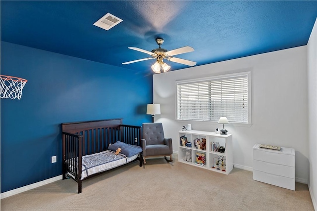 bedroom with ceiling fan, light colored carpet, a textured ceiling, and a nursery area