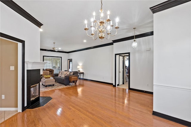 living room with ceiling fan with notable chandelier, ornamental molding, a tile fireplace, and light hardwood / wood-style flooring