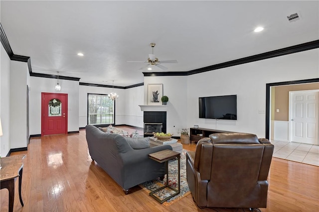 living room featuring ceiling fan with notable chandelier, light hardwood / wood-style floors, crown molding, and a tiled fireplace