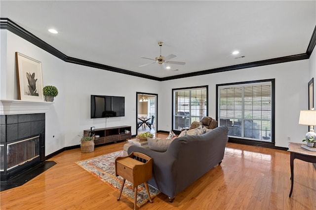 living room with a tiled fireplace, ceiling fan, ornamental molding, and light wood-type flooring