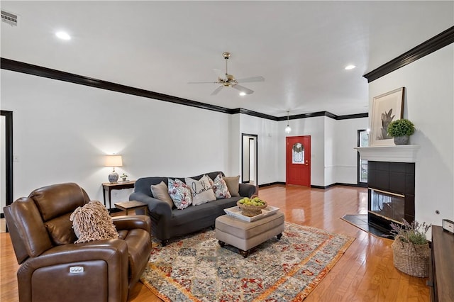 living room with hardwood / wood-style floors, ceiling fan, crown molding, and a tile fireplace