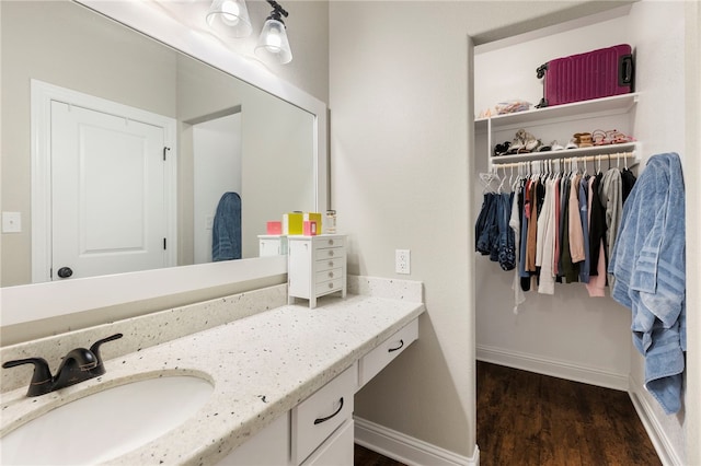 bathroom with a spacious closet, vanity, baseboards, and wood finished floors