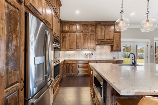 kitchen with hanging light fixtures, appliances with stainless steel finishes, a sink, and decorative backsplash