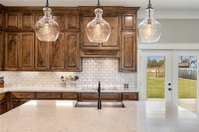 kitchen featuring crown molding, a sink, backsplash, and light stone countertops