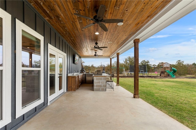 view of patio / terrace featuring a trampoline, french doors, a playground, a ceiling fan, and exterior kitchen