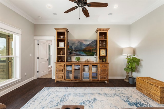 living area featuring dark wood-type flooring, crown molding, baseboards, and a ceiling fan