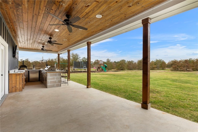 view of patio featuring a trampoline, a playground, an outdoor kitchen, a ceiling fan, and a grill