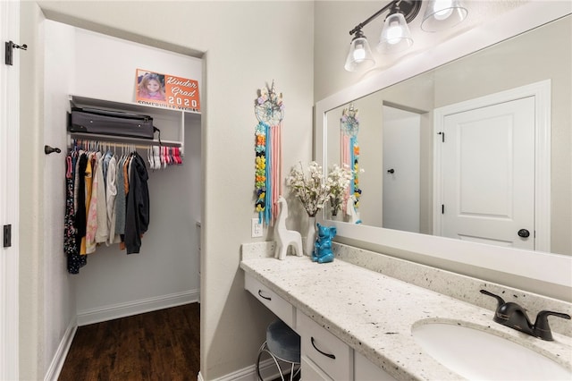 bathroom with baseboards, a walk in closet, wood finished floors, and vanity