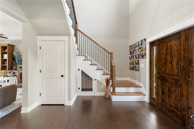 entryway featuring ceiling fan, wood finished floors, a towering ceiling, baseboards, and stairway