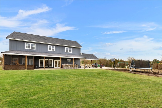 back of property featuring a patio area, roof with shingles, a trampoline, and a yard