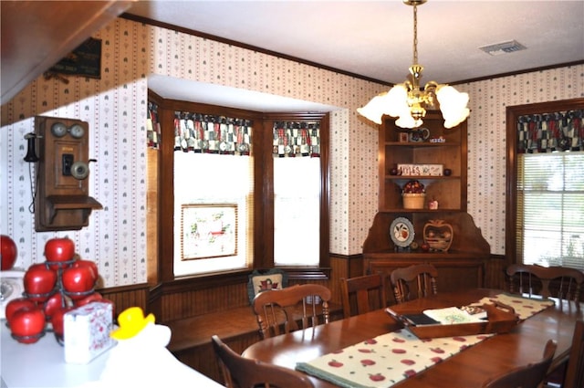 dining space featuring wood walls, ornamental molding, and an inviting chandelier