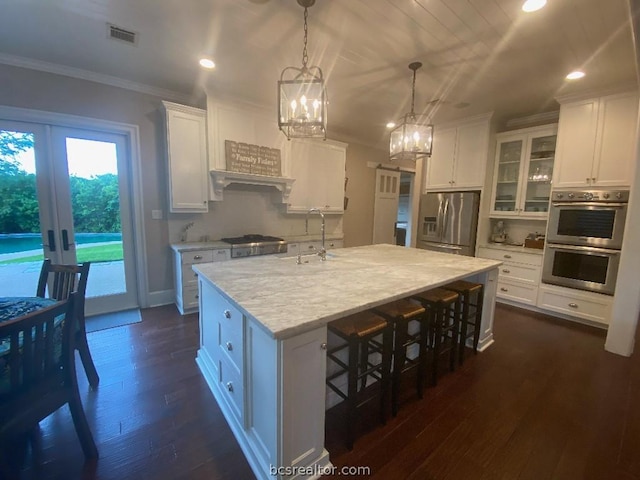 kitchen with french doors, white cabinets, hanging light fixtures, an island with sink, and appliances with stainless steel finishes