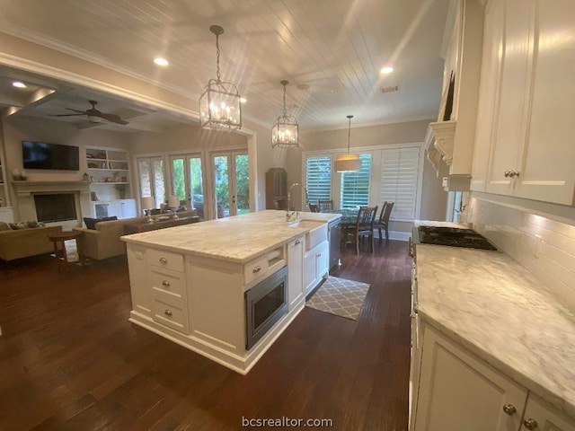 kitchen with light stone countertops, dark hardwood / wood-style flooring, a wealth of natural light, decorative light fixtures, and an island with sink