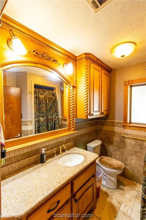 bathroom with tile walls, vanity, a textured ceiling, and toilet