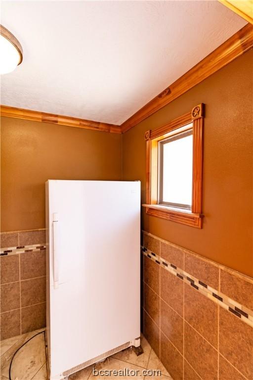 bathroom with tile patterned flooring, crown molding, and tile walls