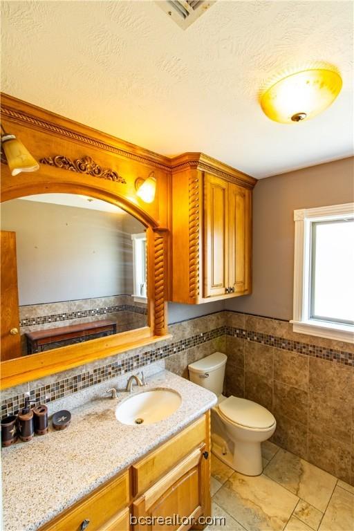 bathroom with vanity, toilet, and tile walls