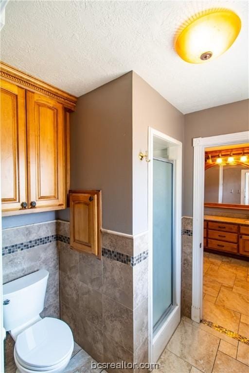 bathroom with a textured ceiling, a shower with door, and tile walls