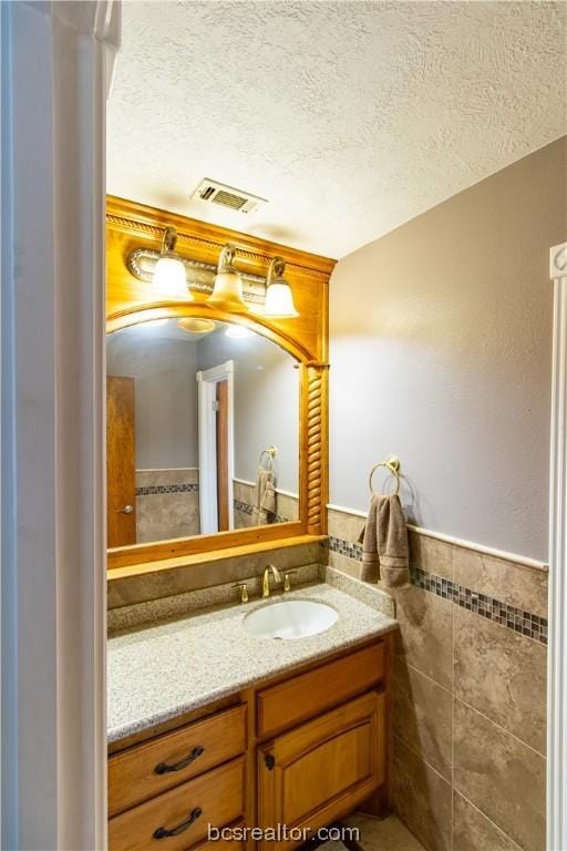 bathroom featuring a textured ceiling, vanity, and tile walls