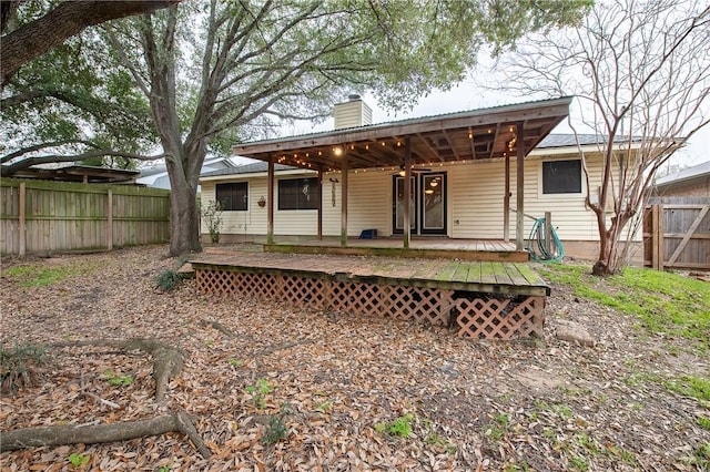 back of property featuring a chimney, fence, metal roof, and a wooden deck