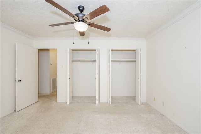 unfurnished bedroom with visible vents, light colored carpet, ornamental molding, a textured ceiling, and multiple closets