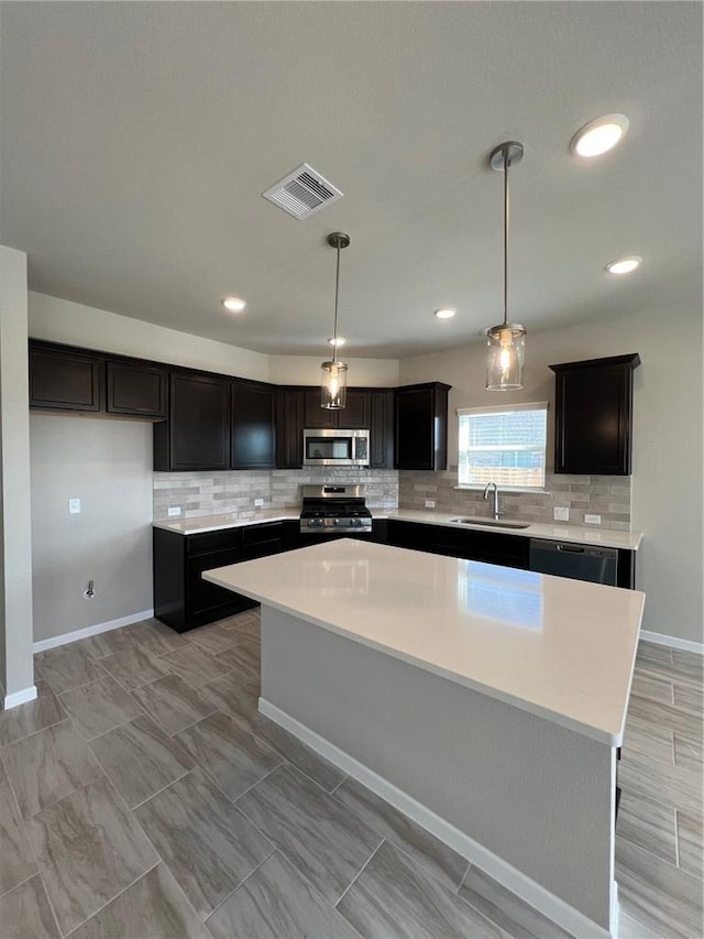 kitchen with stainless steel appliances, decorative light fixtures, sink, and a kitchen island