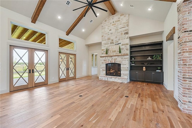 unfurnished living room featuring a stone fireplace, french doors, high vaulted ceiling, and light wood-type flooring