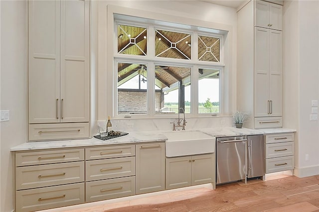 kitchen with light stone countertops, sink, stainless steel dishwasher, and light hardwood / wood-style flooring