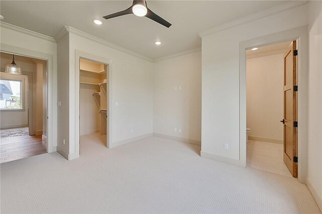 unfurnished bedroom with a walk in closet, light colored carpet, ceiling fan, crown molding, and a closet