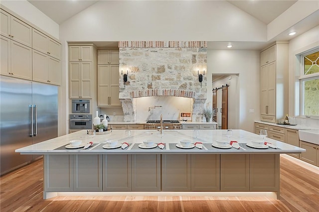 kitchen with light stone countertops, light wood-type flooring, a barn door, and built in fridge