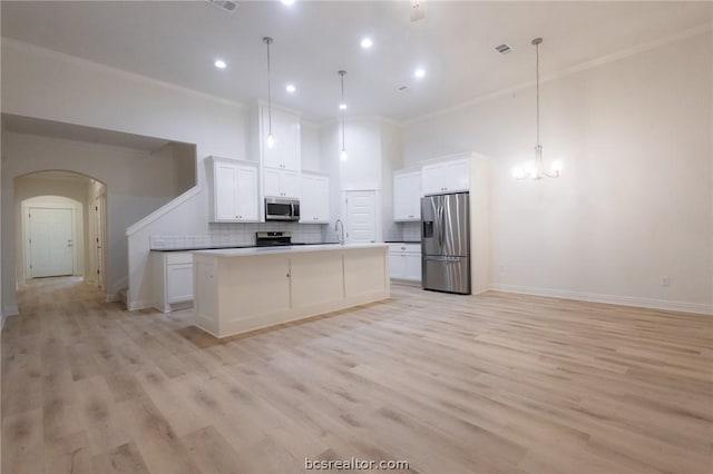 kitchen featuring decorative backsplash, stainless steel appliances, white cabinets, hanging light fixtures, and an island with sink