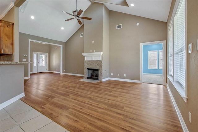 unfurnished living room with light wood finished floors, visible vents, baseboards, a fireplace with flush hearth, and a ceiling fan